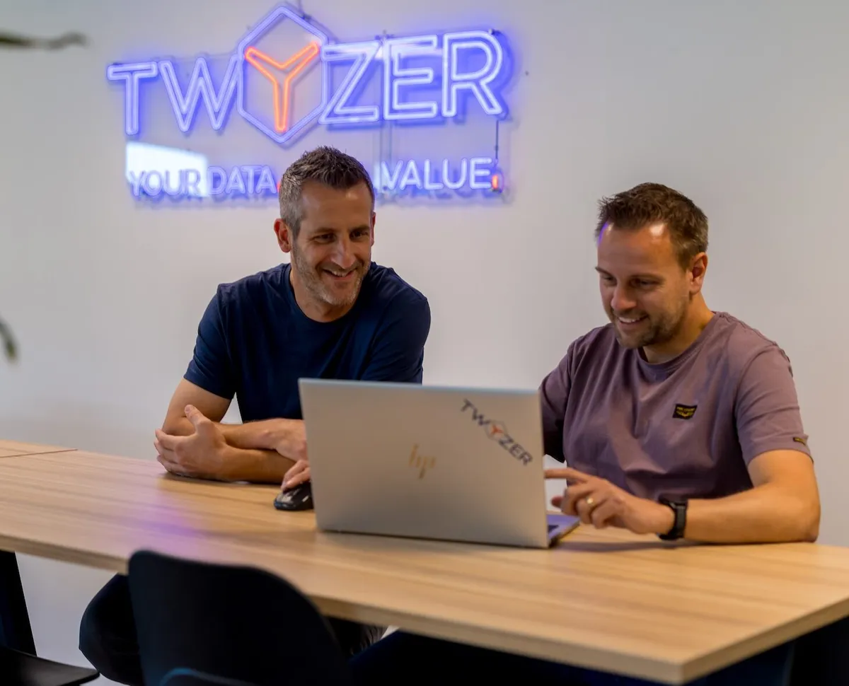 Don van Meel en Perry Lambrechts aan het werk Don van Meel en Perry Lambrechts werken samen achter een laptop in het Twyzer-kantoor met neon logo op de achtergrond