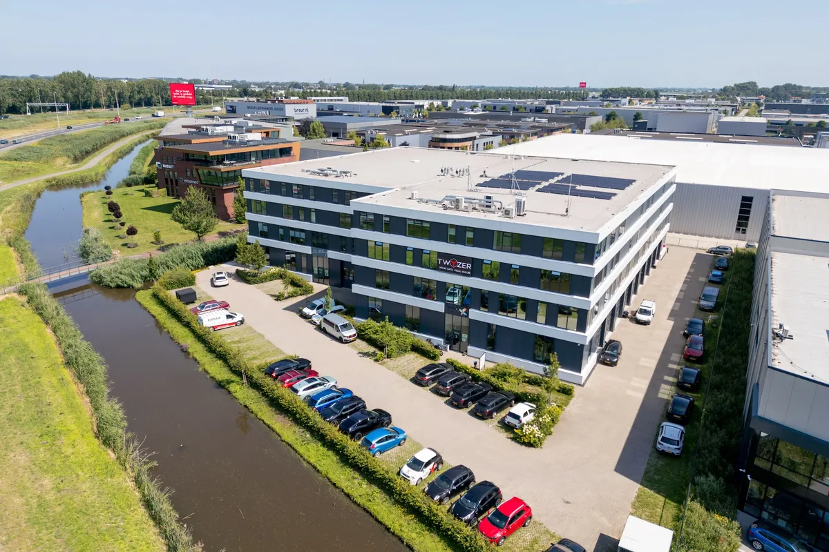 Twyzer kantoor vanuit de lucht Luchtfoto van het Twyzer-kantoorpand met het bedrijfslogo op de gevel, parkeerplaats en kanaal in de omgeving